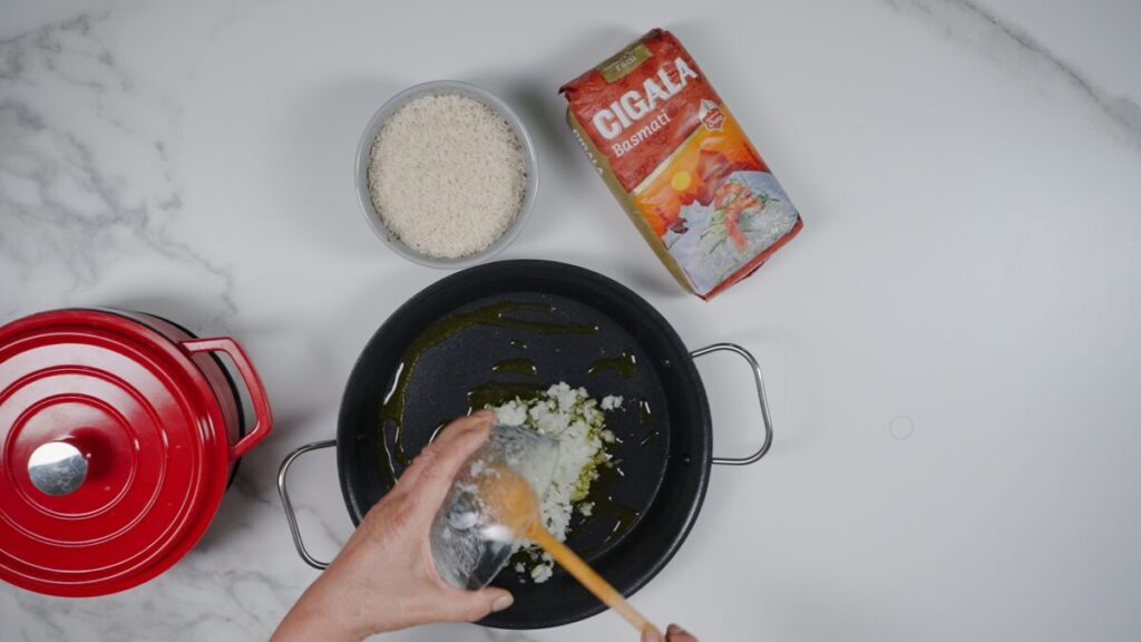 Numa paellera, aqueça um fio de azeite e refogue a cebola até ficar translúcida.